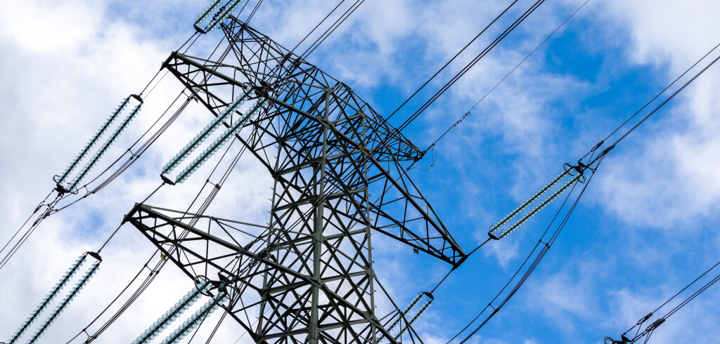 High-voltage pylon against a blue sky with a slight cloud cover. High voltage transmission lines silhouette