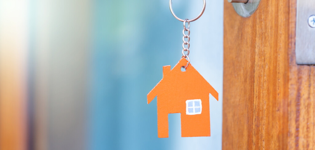 House key in the door with with house shaped keychain.